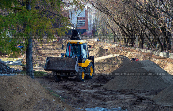 Backhoe loader drives past heaps of soil and dug trenches. Background with tractor at the construction site. Стоковое фото, фотограф Бузмакова Светлана / Фотобанк Лори