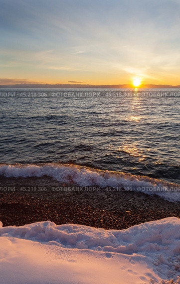 Baikal Lake in December at sunset. Snowy beach in Listvyanka village against backdrop of setting sun. Scenic seascape. Natural background. Outdoor recreation and travel along the lake shore. Стоковое фото, фотограф Виктория Катьянова / Фотобанк Лори