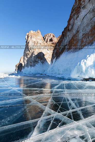 Baikal Lake in sunny cold February day. View of natural landmark of Olkhon Island - famous Cape Sagan-Khushun or Three Brothers Rocks from blue clear ice with cracks. Beautiful winter landscape. Стоковое фото, фотограф Виктория Катьянова / Фотобанк Лори