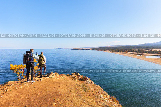 BAIKAL LAKE, OLKHON ISLAND, KHUZHIR VILLAGE, RUSSIA - October 07, 2023: Tourists with backpacks travel around Olkhon Island and admire beautiful view of Saraisky Bay from Burkhan cliff. Редакционное фото, фотограф Виктория Катьянова / Фотобанк Лори