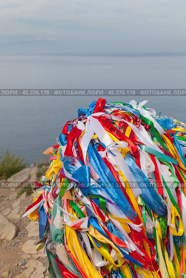 Baikal Lake. The tip of Olkhon Island - northern cape Khoboy attracts many tourists, according to tradition they tie colored ribbons to serge pole. Many colored satin ribbons against background of lake water (2024 год). Стоковое фото, фотограф Виктория Катьянова / Фотобанк Лори