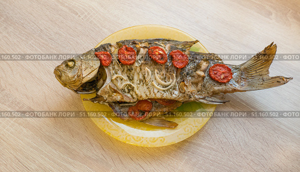 Baked large crucian fish with herbs, tomatoes and spices on a plate on the table. Стоковое фото, фотограф Екатерина Золина / Фотобанк Лори