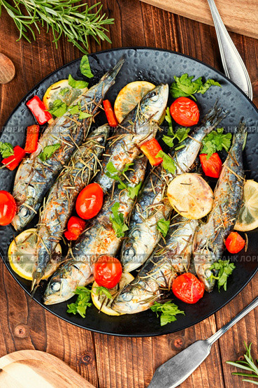 Baked sardine fish with lemon, cherry tomatoes and rosemary on rustic wooden table. Healthy and tasty dinner. Rustic style.. Grilled sardines on a plate with lemon. Стоковое фото, агентство Ingram Publishing / Фотобанк Лори