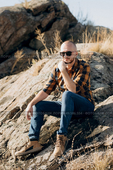 bald guy with a beard in jeans warm shirt and trekking shoes on granite rocks. Стоковое фото, агентство Ingram Publishing / Фотобанк Лори