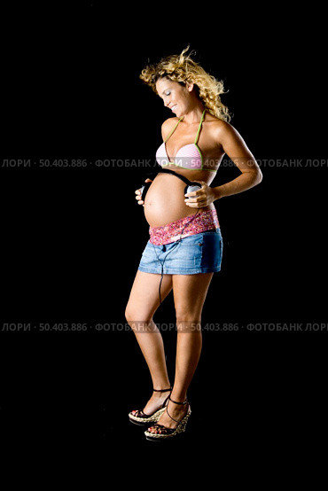Beautiful and young pregnant woman holding a head-phones over her belly to the baby can listen music. Стоковое фото, агентство Ingram Publishing / Фотобанк Лори