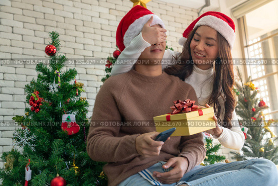beautiful asian girl give surprise christmas gift to her boyfriend in Christmas holiday season greeting. Стоковое фото, агентство Ingram Publishing / Фотобанк Лори