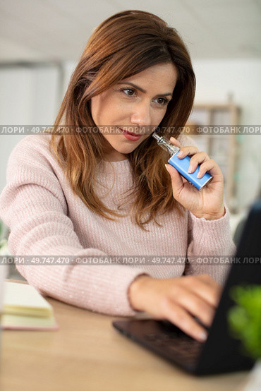 beautiful brunette smoke electronic cigarette and working on her laptop. Стоковое фото, агентство Ingram Publishing / Фотобанк Лори