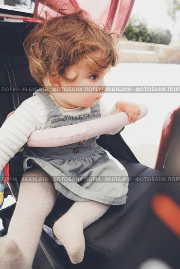 Beautiful little girl with curly hair sitting in her stroller. Стоковое фото, агентство Ingram Publishing / Фотобанк Лори