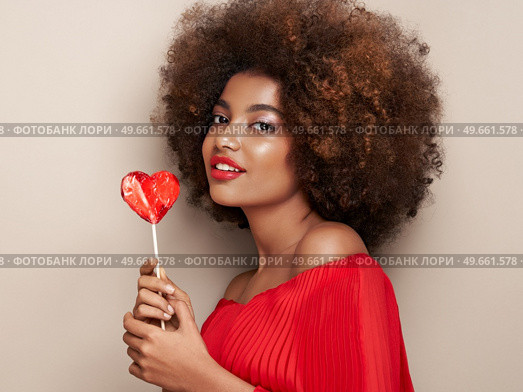 Beautiful portrait of an African girl with a heart shaped lollipop. Valentine’s Day. Symbol of love. Стоковое фото, агентство Ingram Publishing / Фотобанк Лори