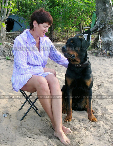 Beautiful woman sitting on the beach on the river with a Rottweiler dog on a summer day. Стоковое фото, фотограф Акиньшин Владимир / Фотобанк Лори