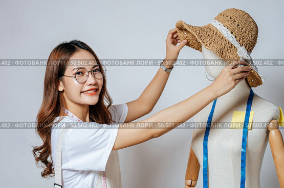 Beautiful young Asian fashion designer or costume smile while design a beautiful sombrero and taking on mannequin. Стоковое фото, агентство Ingram Publishing / Фотобанк Лори