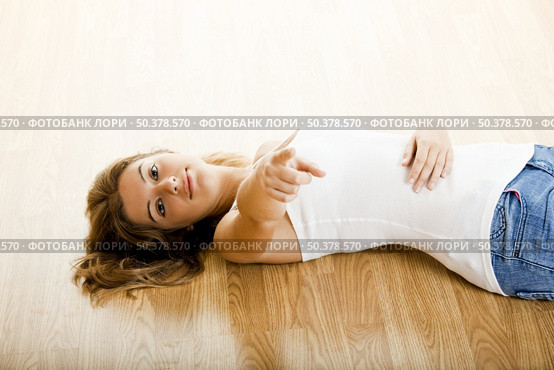 Beautiful young woman lying on floor and pointing to you. Стоковое фото, агентство Ingram Publishing / Фотобанк Лори
