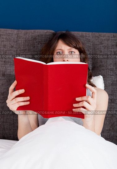 Beautiful young woman reading a book with a astonish expression. Стоковое фото, агентство Ingram Publishing / Фотобанк Лори