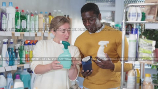 Before buying in household shop, African male customer with European wife choose glass cleaner spray. Стоковое видео, видеограф Яков Филимонов / Фотобанк Лори