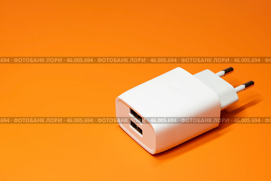 Белый блок питания с двумя портами USB без кабеля на оранжевом фоне. Адаптер питания, зарядное устройство для бытовой электроники. Редакционное фото, фотограф Sergei Gorin / Фотобанк Лори