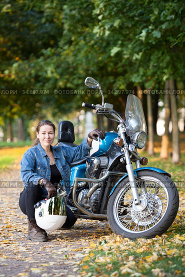 Biker woman with white helmet and jeans outfit portrait, sitting close to motorbike, autumn park. Стоковое фото, фотограф Кекяляйнен Андрей / Фотобанк Лори