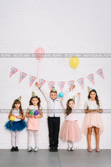 birthday boy standing with girls against white wall decorated with bunting. Стоковое фото, агентство Ingram Publishing / Фотобанк Лори