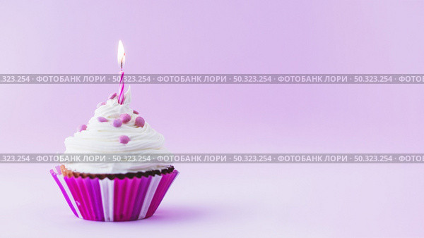 birthday cupcake with illuminated candle purple background. Стоковое фото, агентство Ingram Publishing / Фотобанк Лори
