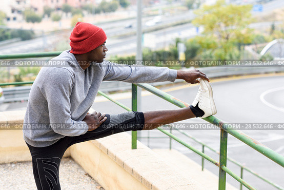 Black man doing stretching before running outdoors. Young male exercising with city scape at the background. Стоковое фото, фотограф Javier Sánchez Mingorance / Ingram Publishing / Фотобанк Лори