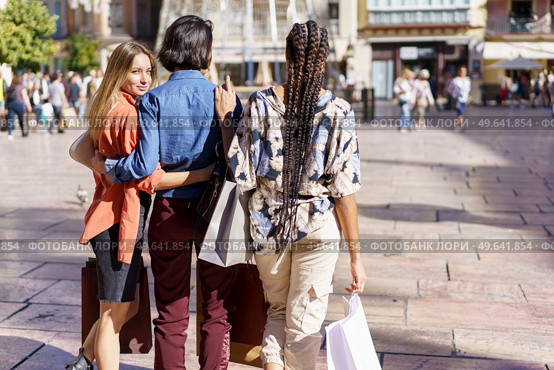 Blond lady with unrecognizable multiracial female friends walking on street pavement after shopping on sunny day. Diverse women walking on street with paper bags. Стоковое фото, агентство Ingram Publishing / Фотобанк Лори