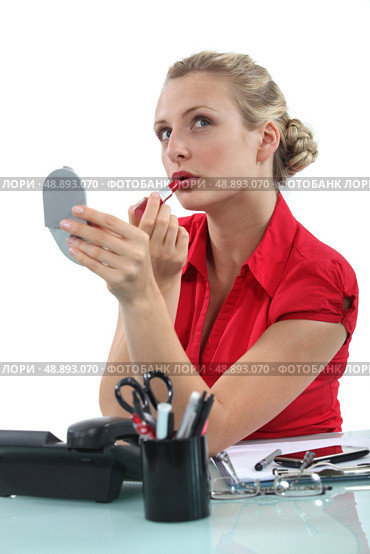 Blond secretary applying lip-stick at her desk. Стоковое фото, агентство Ingram Publishing / Фотобанк Лори