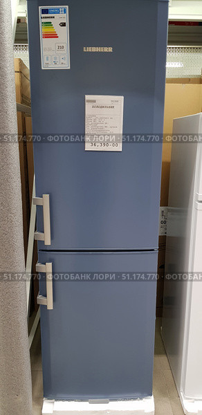 Blue Liebherr refrigerator with a bottom freezer. The model is presented in the sales area, on the door you can see a label with the characteristics and price - 36,390 rubles. The refrigerator has a modern design with straight lines and two separate handles for the upper and lower doors. On the side there is a label with an energy class A++, which indicates high energy efficiency. The total volume of the refrigerator is 210 liters, of which the freezer takes up 84 liters. The color scheme in a sky-blue shade gives the equipment a stylish and unusual appearance, standing out against the background of standard white models. (2018 год). Редакционное фото, фотограф Анна Кривицкая / Фотобанк Лори
