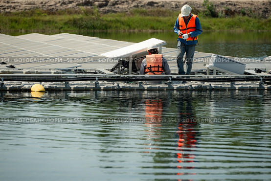 Both of technicians are currently evaluating and repairing the transmission terminals for electricity generated by solar energy in a floating solar power system. Стоковое фото, агентство Ingram Publishing / Фотобанк Лори