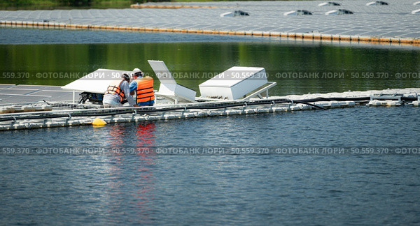 Both of technicians are currently evaluating and repairing the transmission terminals for electricity generated by solar energy in a floating solar power system. Стоковое фото, агентство Ingram Publishing / Фотобанк Лори