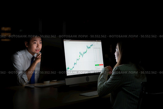 Both of young Asian broker international stock traders working together on desktop at night office, International financial investment company concept. Стоковое фото, агентство Ingram Publishing / Фотобанк Лори