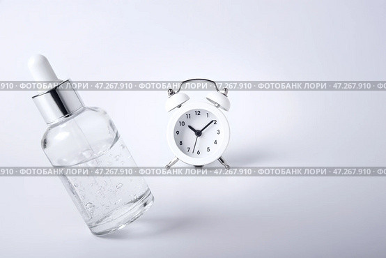 Bottle of face serum levitates on a white background next to the retro alarm clock. Стоковое фото, фотограф София Тюленева / Фотобанк Лори