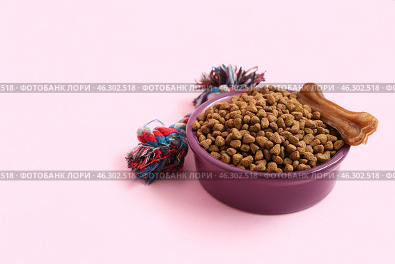 Bowl with dry food, bone and chew toy on pink background. Стоковое фото, фотограф Pixel_shot / Фотобанк Лори