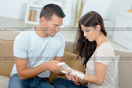 boyfriend helping girlfriend with fractured hand sitting on sofa. Стоковое фото, агентство Ingram Publishing / Фотобанк Лори