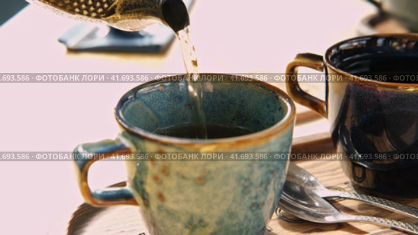 Brewing and Serving Tea. Teapot Pouring Green Tea in Blue Ceramic Cup on Wooden Cafe Table. Two Pottery Handmade Mugs Early in the Morning. Trendy Authentic Porcelain Set. Breakfast Concept. Tea Time. Стоковое видео, видеограф Марина Демидюк / Фотобанк Лори