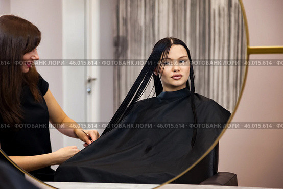 Brunette woman visit hairdresser, sitting on barber chair, looking at mirror. Hairstylist making fashionable hairstyle in barber shop. Customer service at hair salon, haircare. Copy ad text space. Стоковое фото, фотограф Aleksandr Golubev / Фотобанк Лори