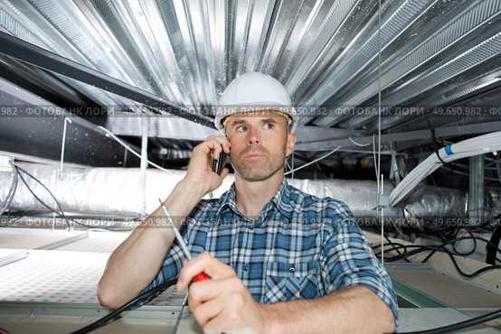 builder on cell phone crouching on elevated scaffolding near ceiling. Стоковое фото, агентство Ingram Publishing / Фотобанк Лори