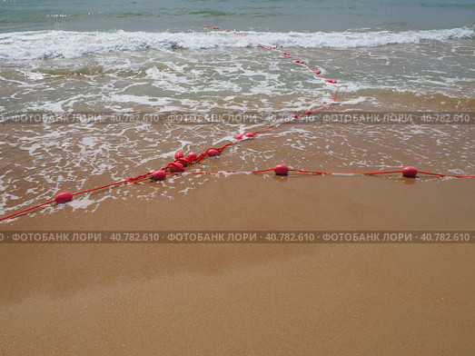 Buoys on a rope in sea water. The lifebuoys are pink restraints to alert people to the depth of the water. Rescue of the drowning. Delimiting a place on sandy beach between hotels. Wave with bubbles. Стоковое фото, фотограф Юлия Петровская / Фотобанк Лори