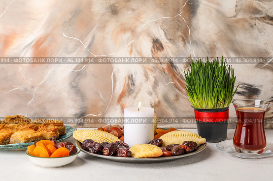 Burning candle with treats, grass and glass of tea on table near grunge wall. Novruz Bayram celebration. Стоковое фото, фотограф Pixel_shot / Фотобанк Лори