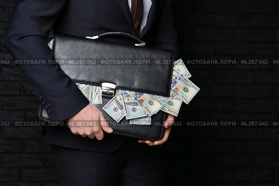 Businessman holding briefcase with dollar banknotes on dark background. Corruption concept. Стоковое фото, фотограф Pixel_shot / Фотобанк Лори