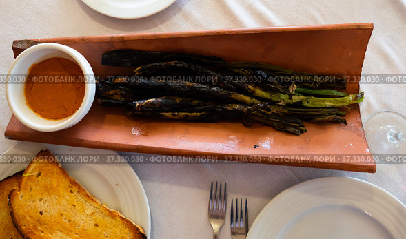 Calcots onions served on plate with Romesco sauce - traditional Catalan dish. Стоковое фото, фотограф Яков Филимонов / Фотобанк Лори