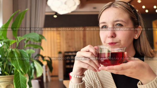 Calm happy girl sitting by the window in cafe, holding cup of hot black tea. Relaxation, happiness, peace. Стоковое видео, видеограф Сахарова Мария Юрьевна / Фотобанк Лори