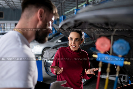 Car mechanic working in an auto repair shop explain to customer after inspecting the operation of the car’s air conditioner and refrigerant. Стоковое фото, агентство Ingram Publishing / Фотобанк Лори