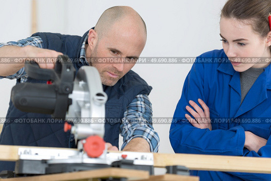 carpenter training female apprentice to use mechanized saw. Стоковое фото, агентство Ingram Publishing / Фотобанк Лори