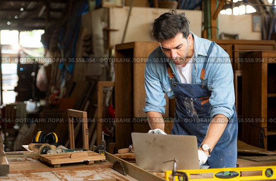 Carpenter working on laptop in his workshop at a woodworking factory. Стоковое фото, агентство Ingram Publishing / Фотобанк Лори