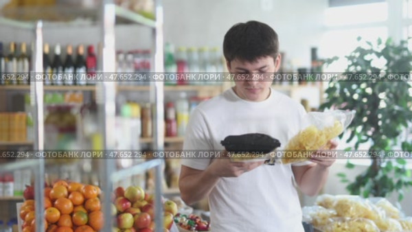 Casually dressed young guy examining two chip bags while shopping for snacks in local grocery store, comparing ingredients and nutritious value before buying. Стоковое видео, видеограф Яков Филимонов / Фотобанк Лори