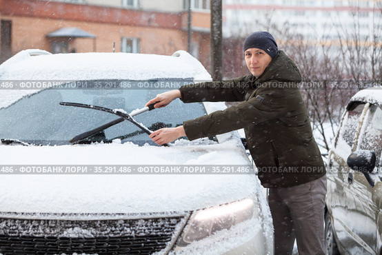 Caucasian driver cleans windshield and removes snow from rubber wipers of his car. Стоковое фото, фотограф Кекяляйнен Андрей / Фотобанк Лори