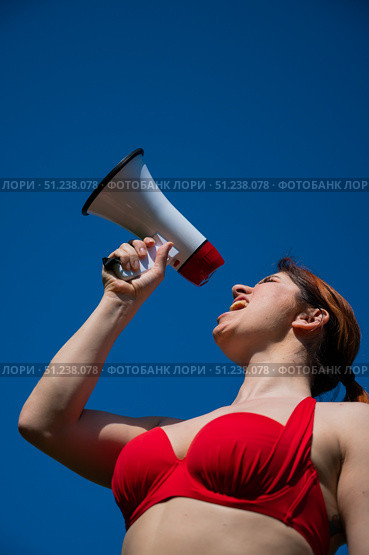 Caucasian woman in red bikini works as a lifeguard on the beach and shouts through a megaphone against a blue sky. A girl in a swimsuit is standing with a loudspeaker. Summer vacation. Стоковое фото, фотограф Михаил Решетников / Фотобанк Лори