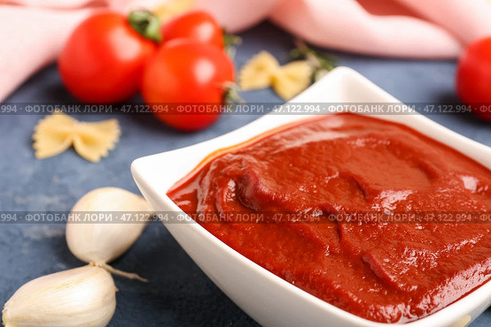 Чаша вкусной томатной пасты, зубчики чеснока и сырые макароны фарфалле на сером фоне гранж. Стоковое фото, фотограф Pixel_shot / Фотобанк Лори