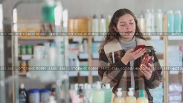 Checking expiration date of liquid hand soap - female shopper in winter clothes scans QR code on label of liquid hand soap using her smartphone. Стоковое видео, видеограф Яков Филимонов / Фотобанк Лори