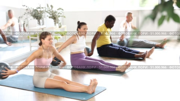 Cheerful young female fitness instructor guiding group Pilates sessions in warm, sunlit studio, performing Around World exercise with ball, enhancing coordination, balance, and flexibility. Стоковое видео, видеограф Яков Филимонов / Фотобанк Лори