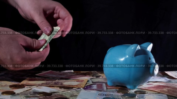 Человек сворачивает американскую долларовую купюру и опускает её в копилку-свинку. Стоковое видео, видеограф Семён Прудий / Фотобанк Лори